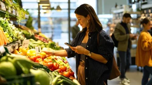 Kundin gleicht digitale Einkaufsliste mit Produkten im modernen Supermarkt ab