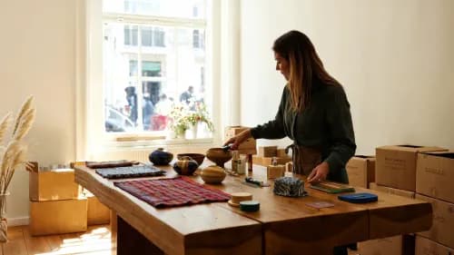 Boutique-Inhaberin sortiert neue Produkte einer B2B-Handelsplattform im hellen Ladengeschäft