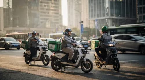 Lieferfahrer auf E-Scootern warten an Kreuzung in chinesischer Großstadt
